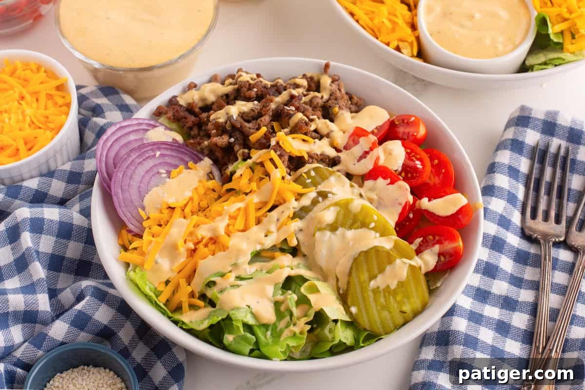 A burger bowl with ground beef, shredded cheddar cheese, dill pickles, cherry tomatoes, red onion, and lettuce, all topped with a creamy homemade burger bowl sauce. 
