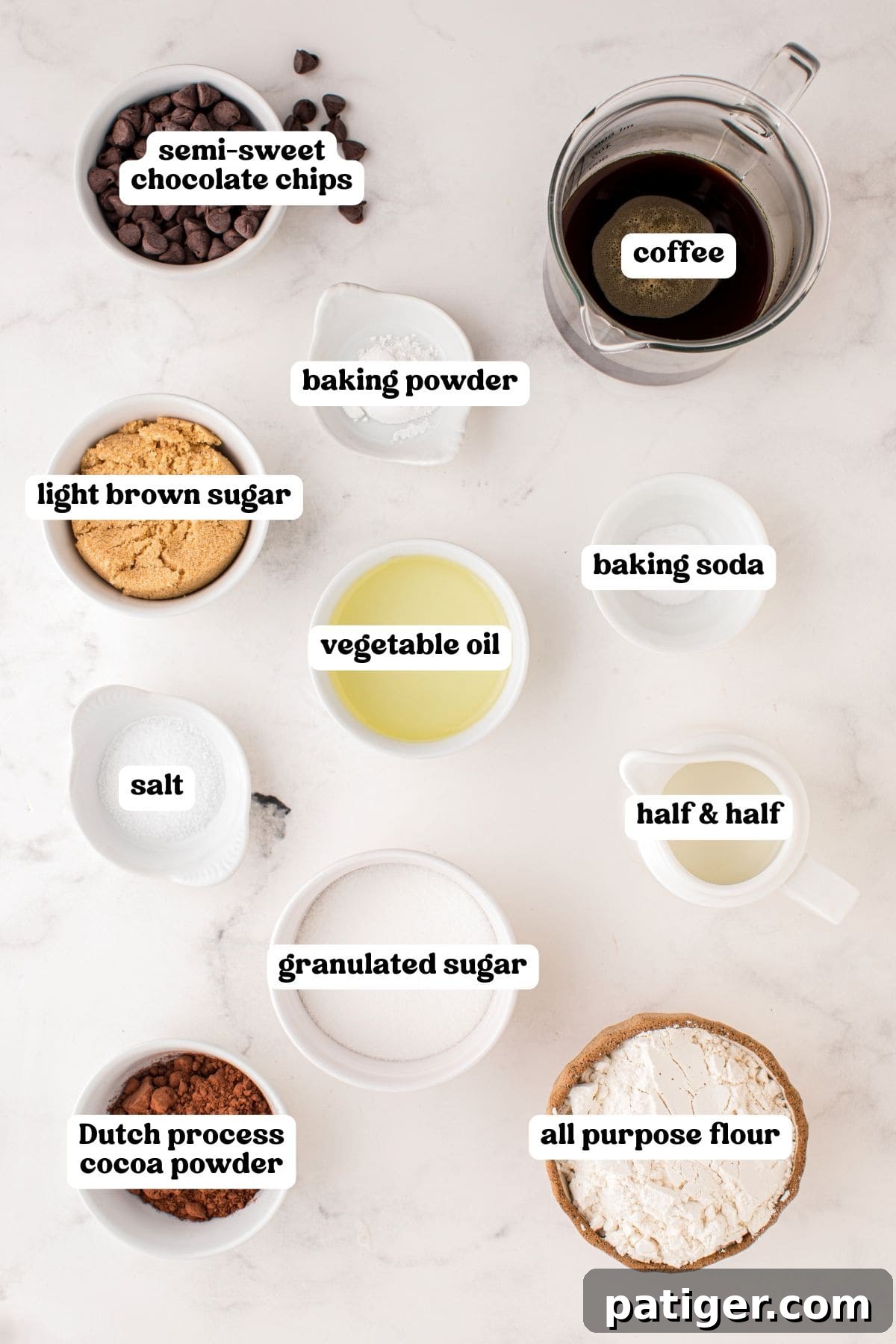 An inviting overhead display of neatly arranged baking ingredients in pristine white bowls. Elements include semi-sweet chocolate chips, freshly brewed coffee in a glass measuring cup, baking powder, light brown sugar, baking soda, vegetable oil, salt, half and half, granulated sugar, Dutch process cocoa powder, and all-purpose flour, all set on a bright, minimalist surface.