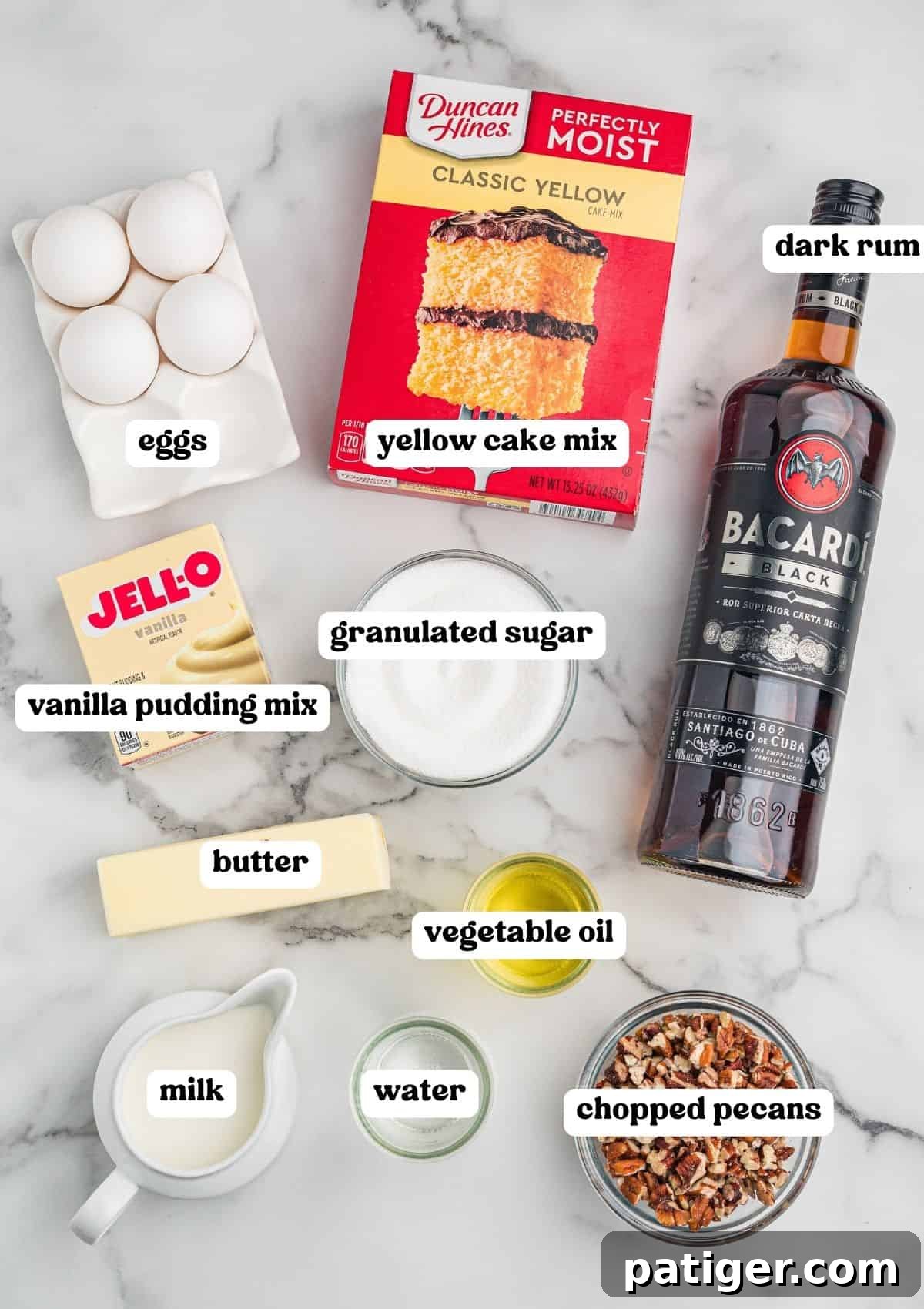 Rum cake ingredients on marble: eggs, yellow cake mix, vanilla pudding, sugar, butter, oil, milk, water, pecans, dark rum.