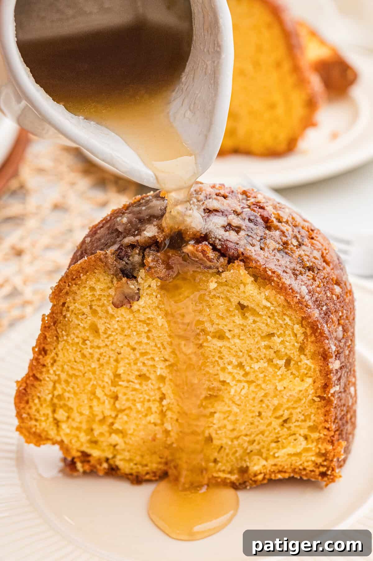 Amber glaze being poured from a small white pitcher onto a slice of rum bundt cake.