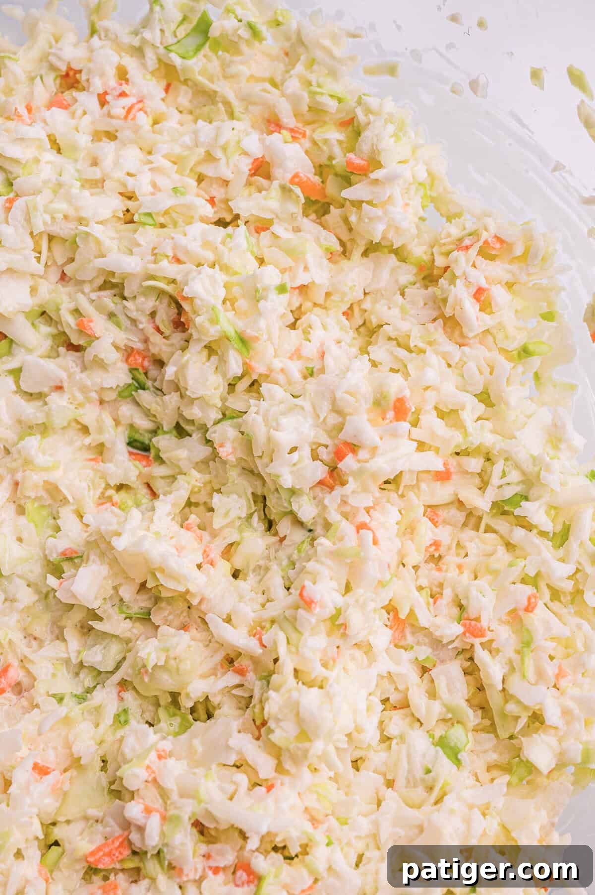 Top-down view of finely shredded cabbage and carrot coleslaw mixed in creamy dressing in a glass bowl.