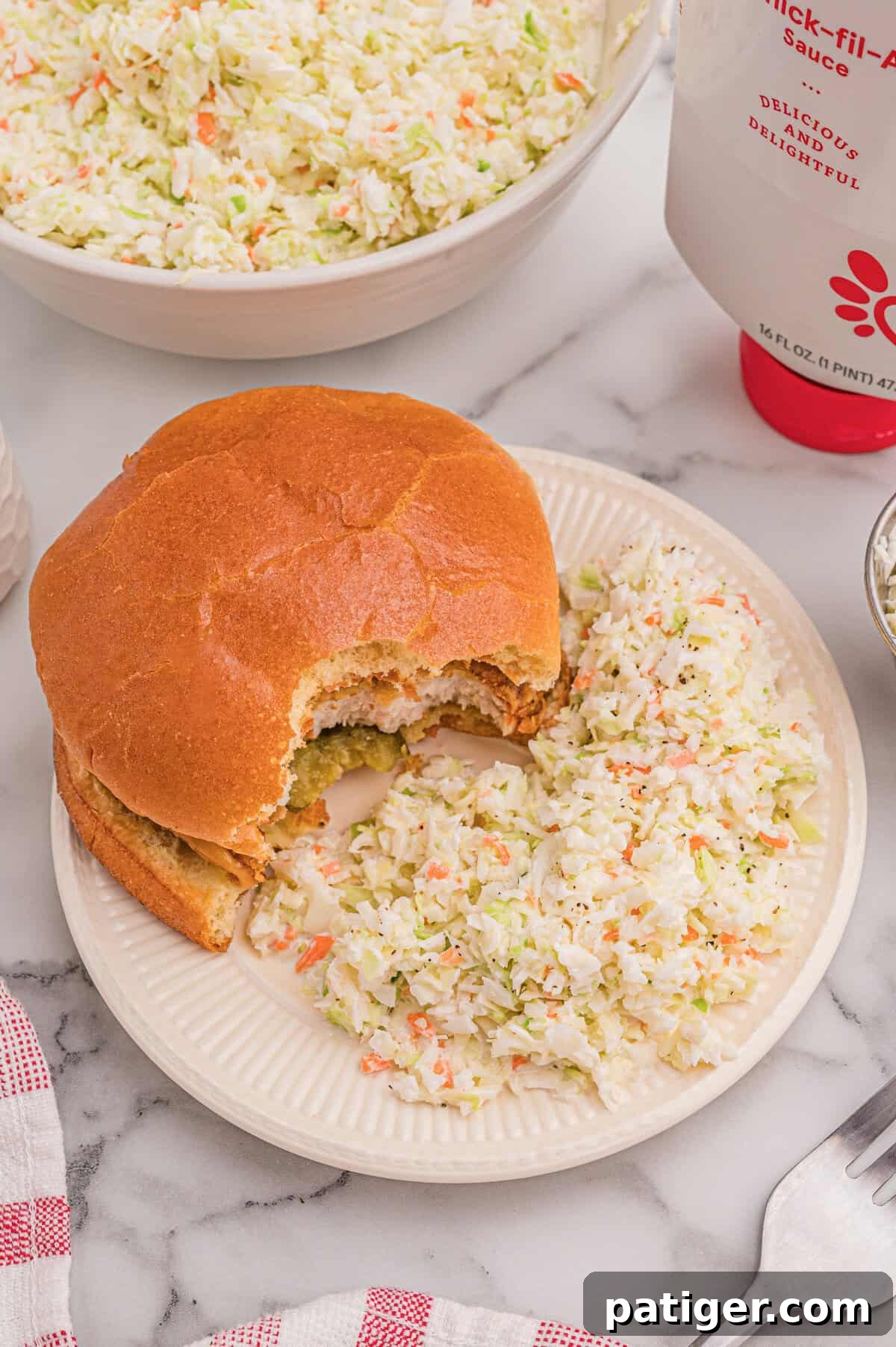 Chicken sandwich plated with coleslaw on the side, a bottle of Chick-fil-A sauce in the background.