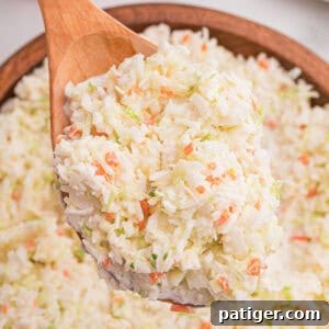 Close-up of a wooden spoon lifting a heaping scoop of finely shredded coleslaw from a wooden bowl.