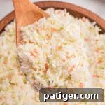 Close-up of a wooden spoon lifting a heaping scoop of finely shredded coleslaw from a wooden bowl.