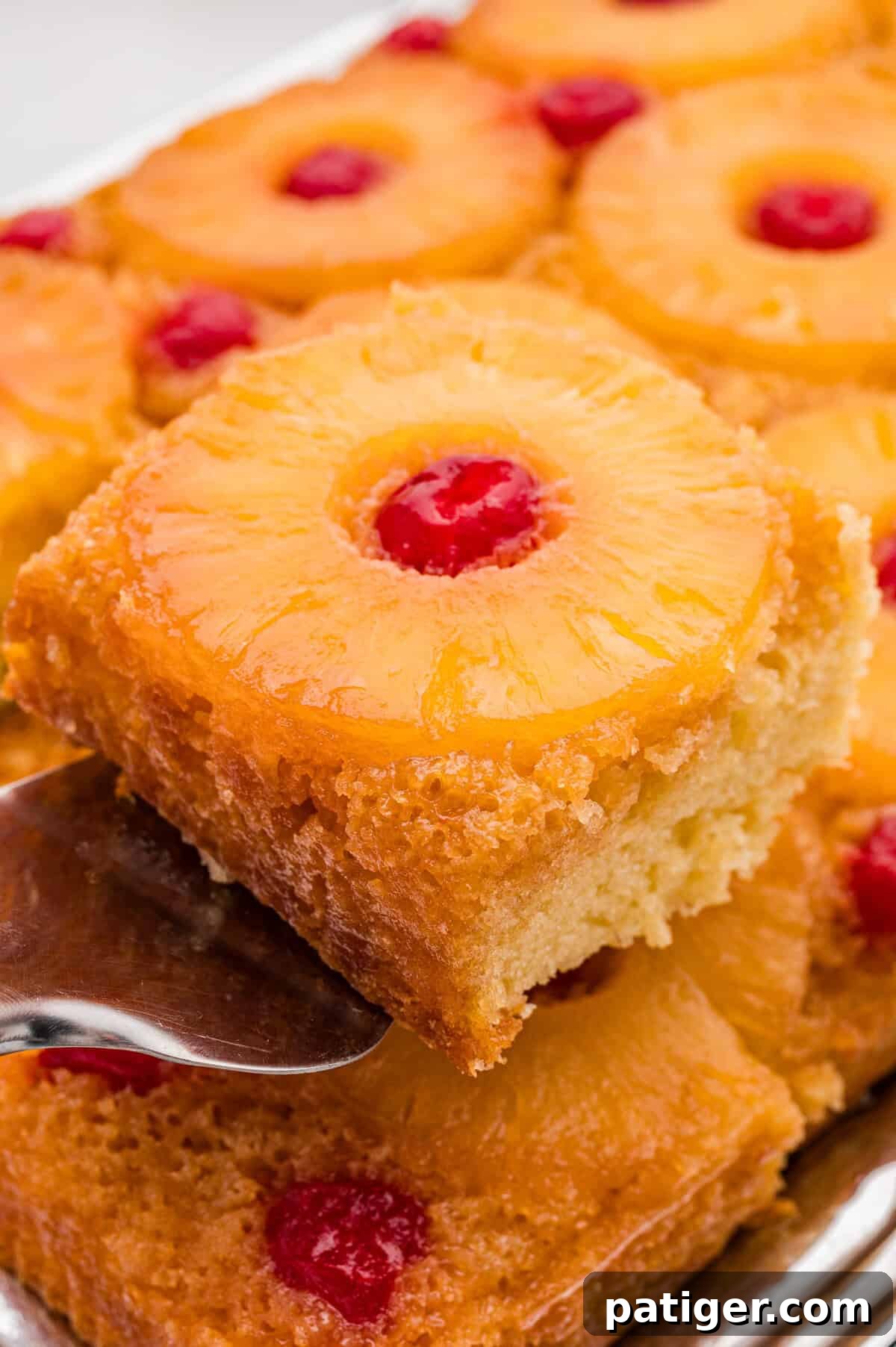 A slice of pineapple upside down cake being lifted on a metal serving spatula from the pan.
