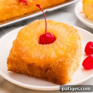 Square plated slice of pineapple upside down cake with a pineapple ring and a cherry on a white dish.