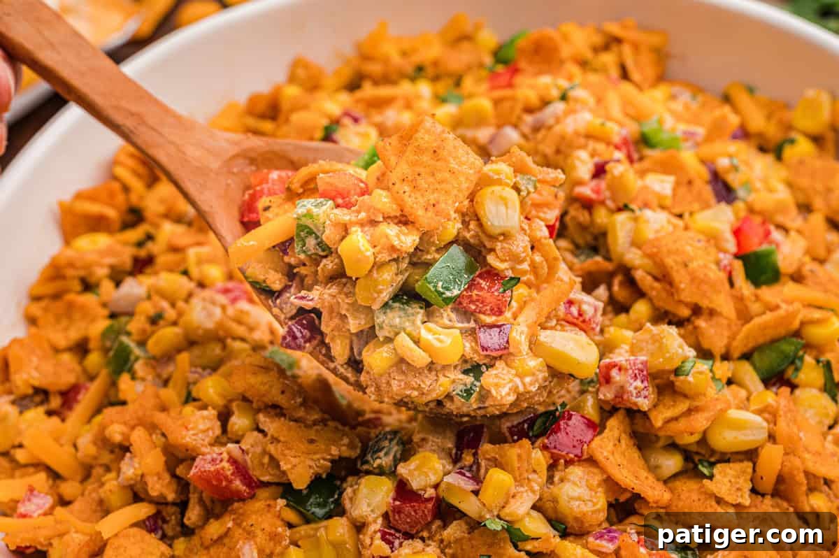 Bowl of Frito corn salad with a wooden spoon.