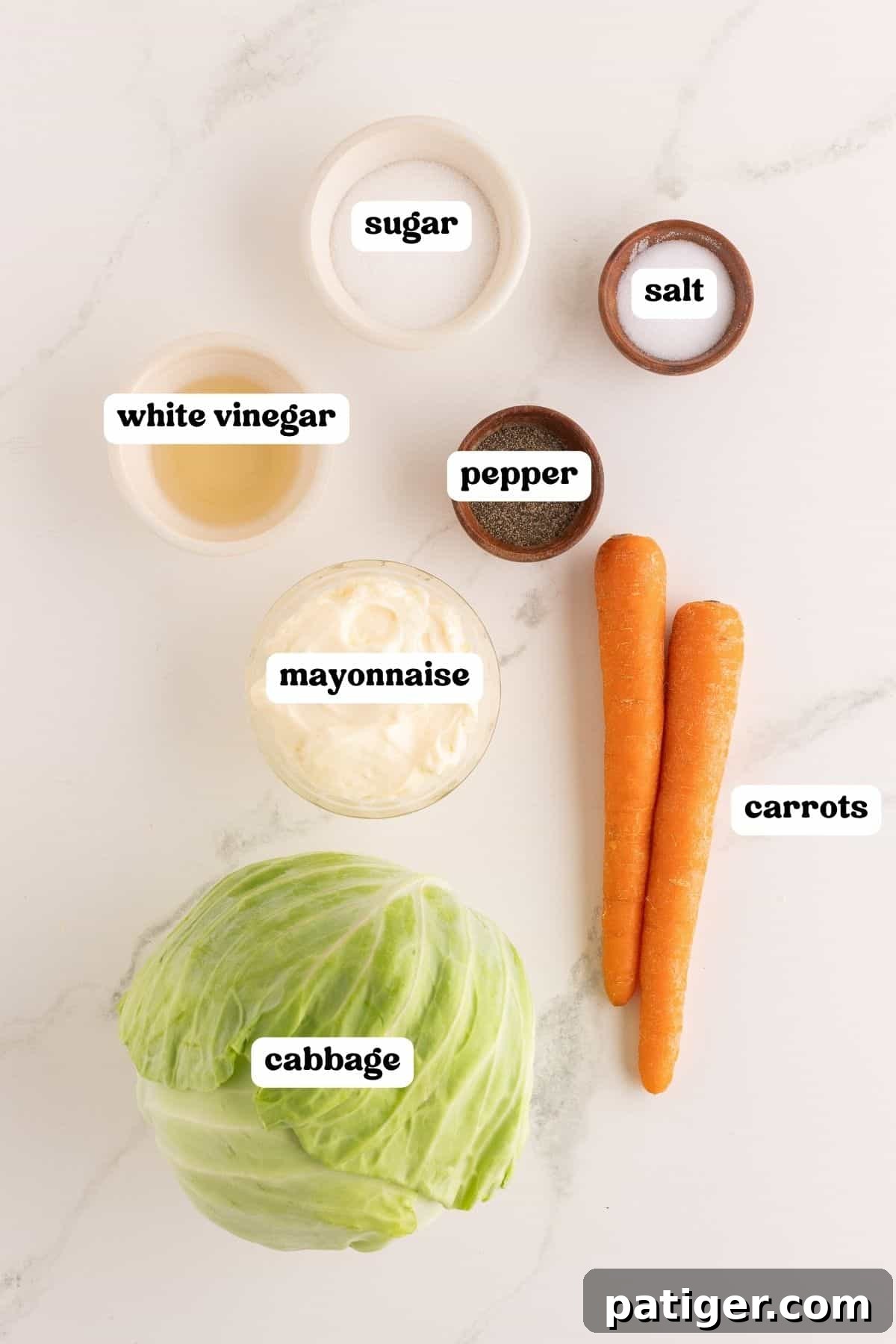 Ingredients on a marble counter: a head of green cabbage, two carrots, white vinegar, mayonnaise, sugar, salt, and pepper.