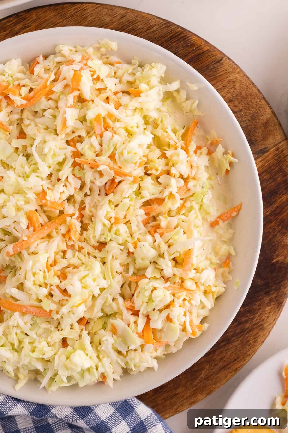 Overhead view of homemade coleslaw in a white bowl with shredded green cabbage and orange carrots tossed in creamy dressing.