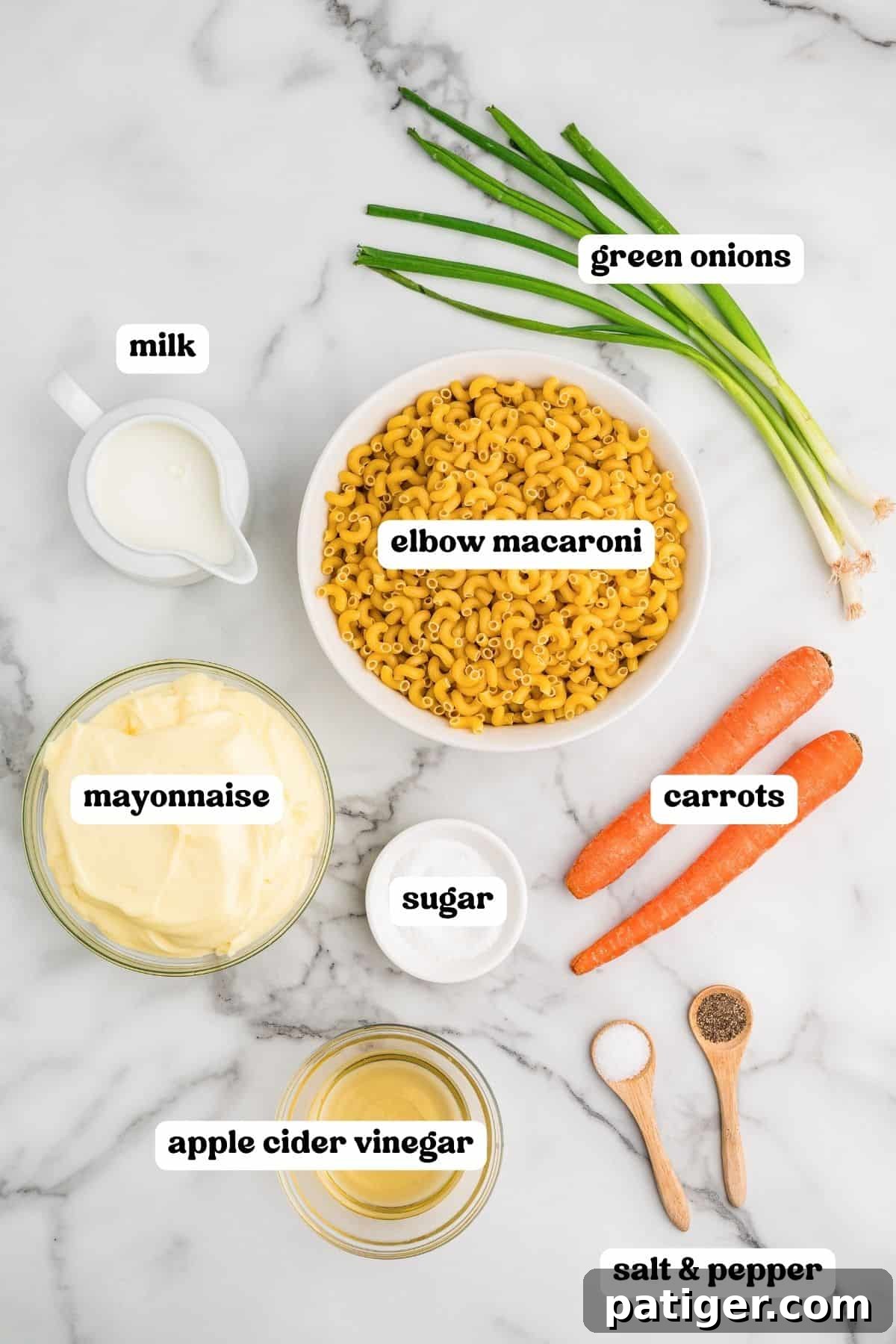 Labeled ingredients on a marble counter: green onions, milk, elbow macaroni, mayonnaise, sugar, carrots, apple cider vinegar, and salt and pepper.