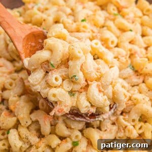 A wooden spoon lifting a scoop of creamy Hawaiian mac salad with shredded carrots and green onion from a bowl.