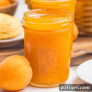 Apricot Jam Without Pectin: Simple Homemade Recipe 10 A close-up of a mason jar filled with apricot jam beside a single whole apricot on a marble counter.