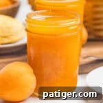 Apricot Jam Without Pectin: Simple Homemade Recipe 11 A close-up of a mason jar filled with apricot jam beside a single whole apricot on a marble counter.