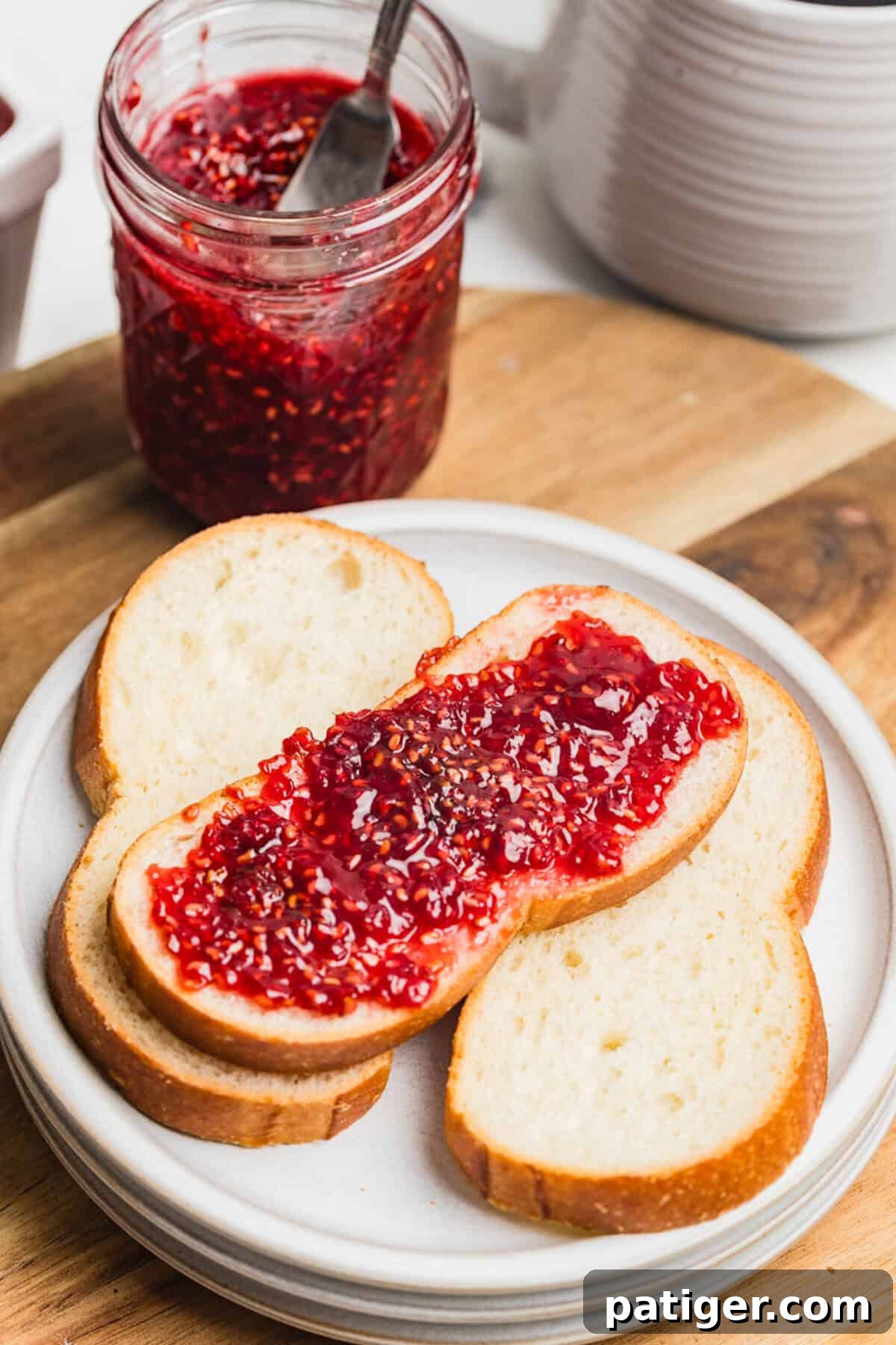 Homemade Raspberry Jam Without Pectin — Simple Stove-Top Recipe 2 A slice of bread spread with raspberry jam on a white plate with a jar of homemade raspberry jam.