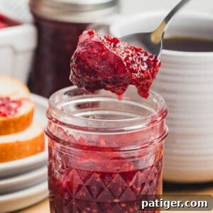 Homemade Raspberry Jam Without Pectin — Simple Stove-Top Recipe 9 A close-up square shot of a spoon lifting raspberry jam from a small mason jar with a slice of bread in the background.