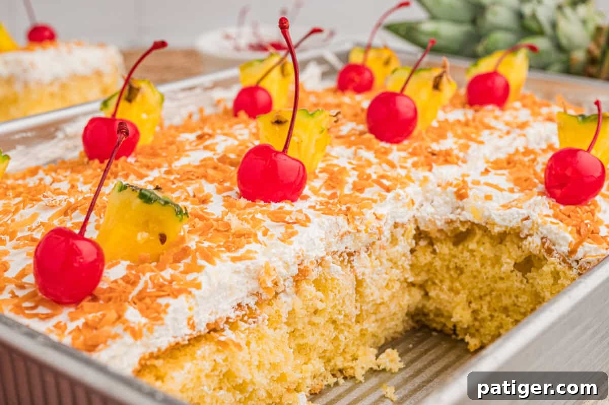 Tropical Piña Colada Layer Cake with Rum-Soaked Pineapple 9 Close-up of the cake in a metal pan, cut into squares and topped with toasted coconut, maraschino cherries, and pineapple wedges.