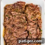 Juicy Slow Cooker Carne Asada Recipe 12 Sliced carne asada in a white baking dish, flecked with cilantro.