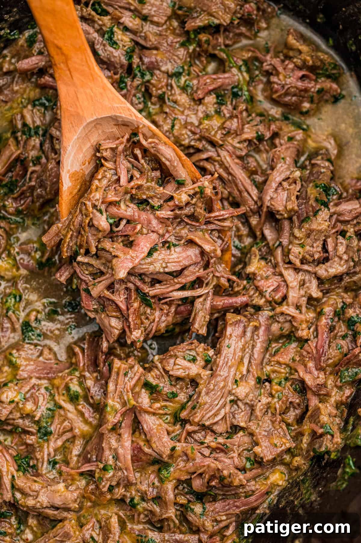Juicy Slow Cooker Carne Asada Recipe 3 A wooden spoon resting in a slow cooker full of saucy shredded beef flecked with cilantro.