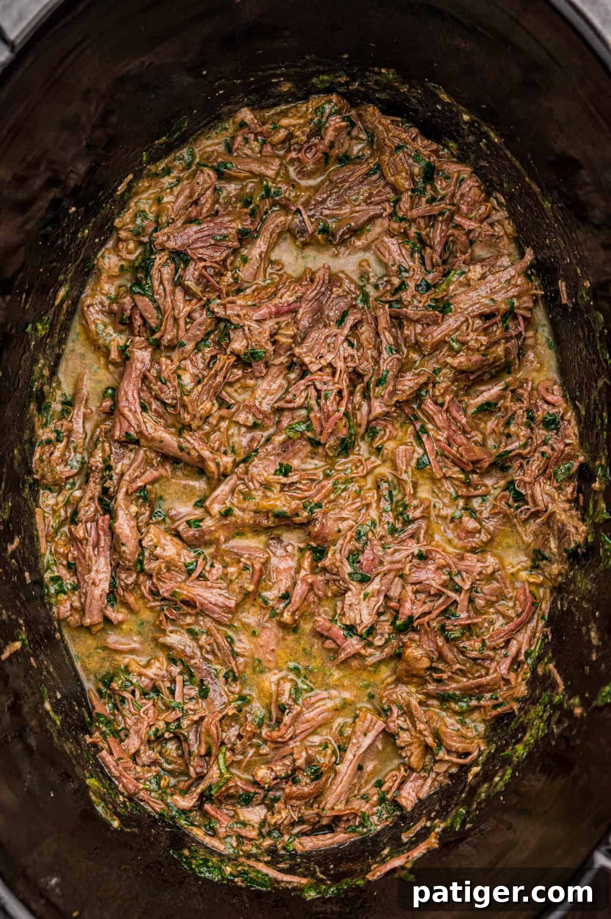 Juicy Slow Cooker Carne Asada Recipe 8 Shredded slow cooker carne asada coated in sauce and flecked with cilantro in a black slow cooker.