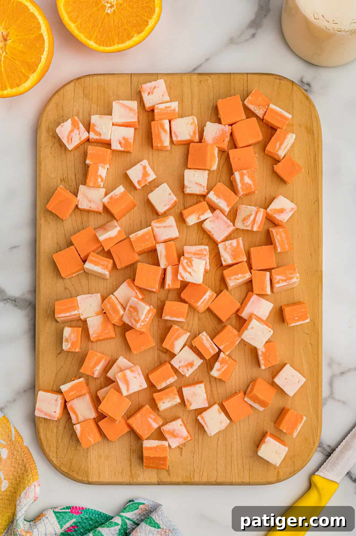 Creamsicle Orange Fudge Recipe 5 Orange creamsicle fudge cut into cubes on a wood board with orange halves and a knife nearby.