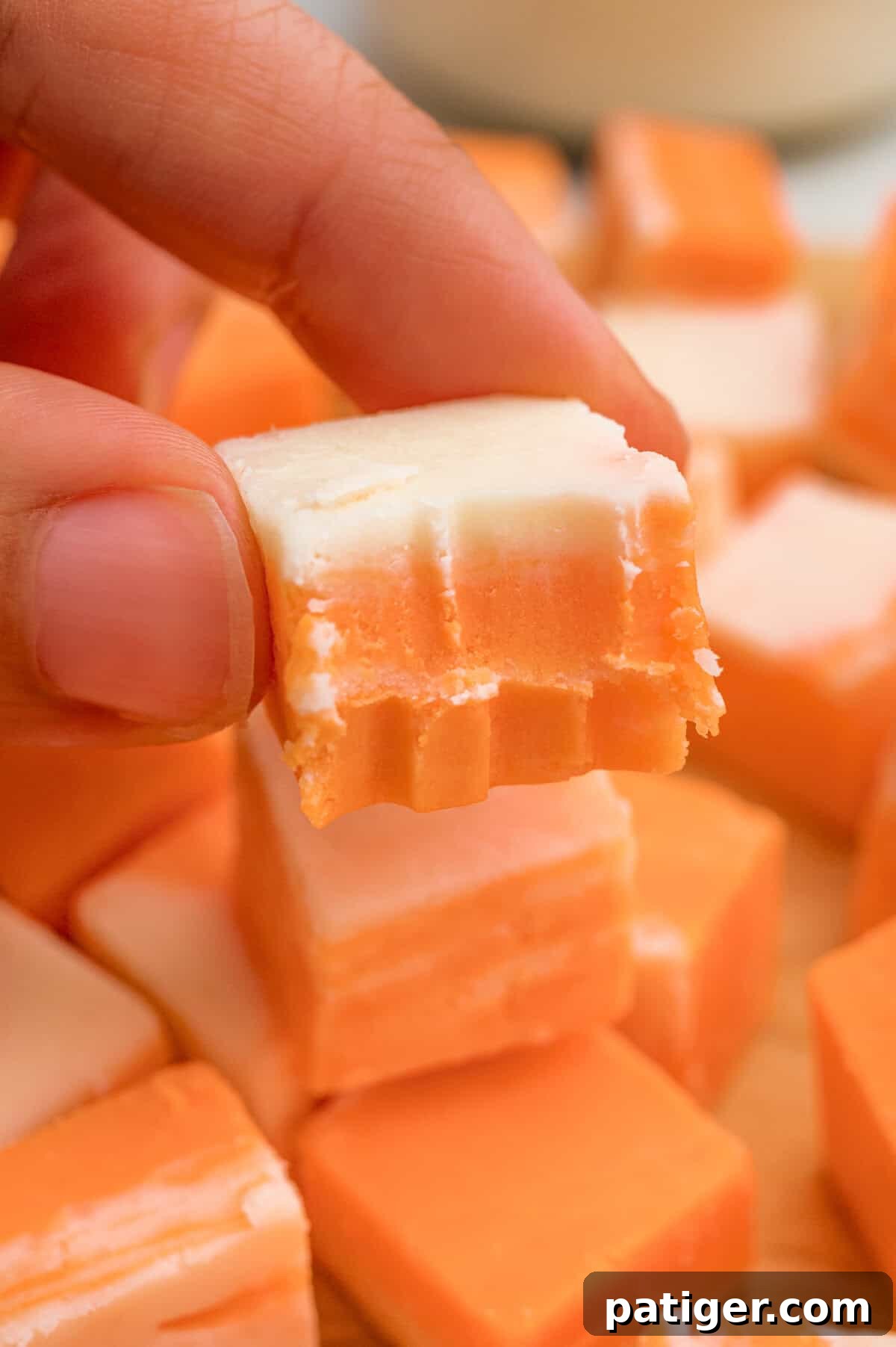 Creamsicle Orange Fudge Recipe 6 A hand holding a square of orange and white fudge with a bite taken out.