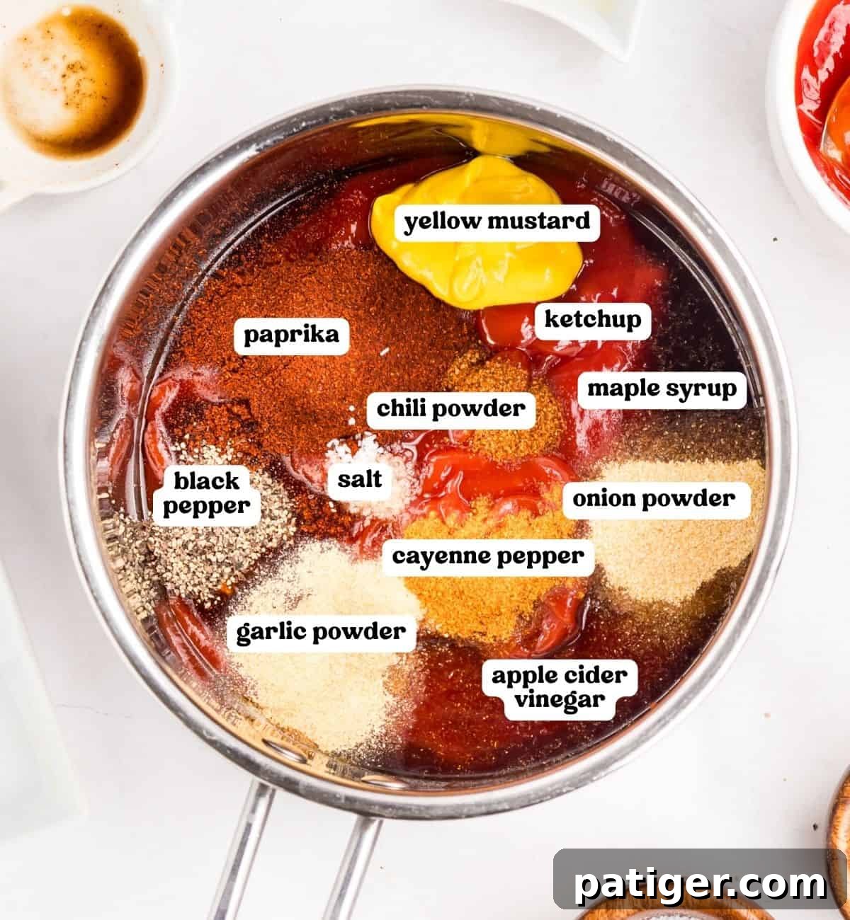 How to Make Tangy Homemade BBQ Sauce 3 Barbecue sauce ingredients in a saucepan with labels: ketchup, yellow mustard, maple syrup, paprika, chili powder, cayenne, salt, black pepper, garlic powder, onion powder, apple cider vinegar.