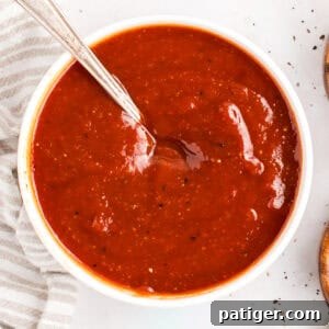 How to Make Tangy Homemade BBQ Sauce 7 Overhead view of homemade BBQ sauce in a white bowl with a spoon resting in it.