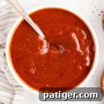 How to Make Tangy Homemade BBQ Sauce 8 Overhead view of homemade BBQ sauce in a white bowl with a spoon resting in it.