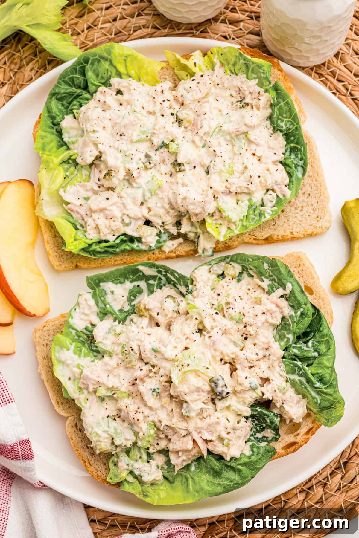 Tuna Salad Recipe for Sandwiches, Wraps, and Lunch 2 Two open-faced tuna salad sandwiches on lettuce and toast with apple slices and pickles nearby.