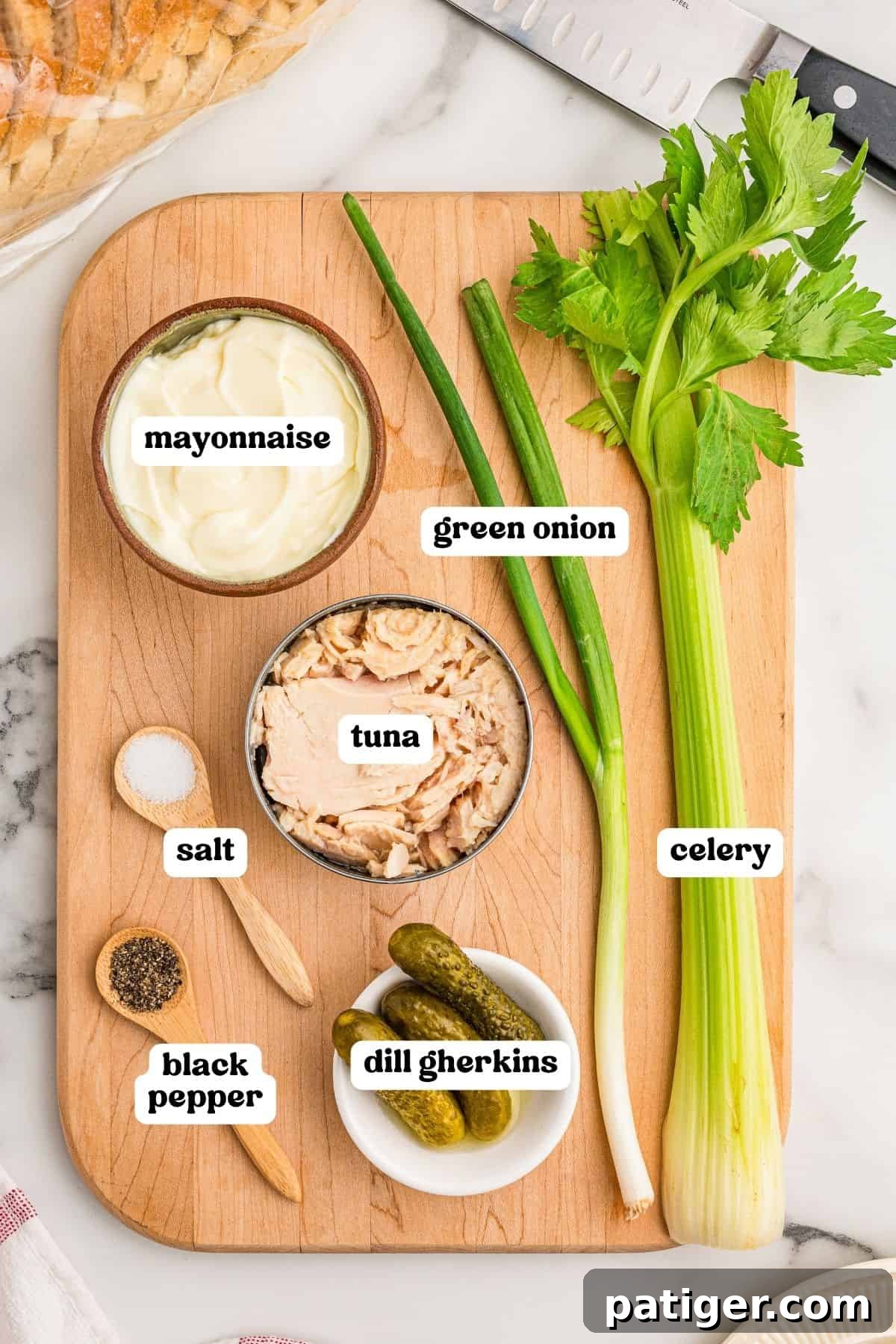 Tuna Salad Recipe for Sandwiches, Wraps, and Lunch 3 Ingredients on a wooden board: mayonnaise, canned tuna, green onion, celery, dill gherkins, salt, and black pepper.
