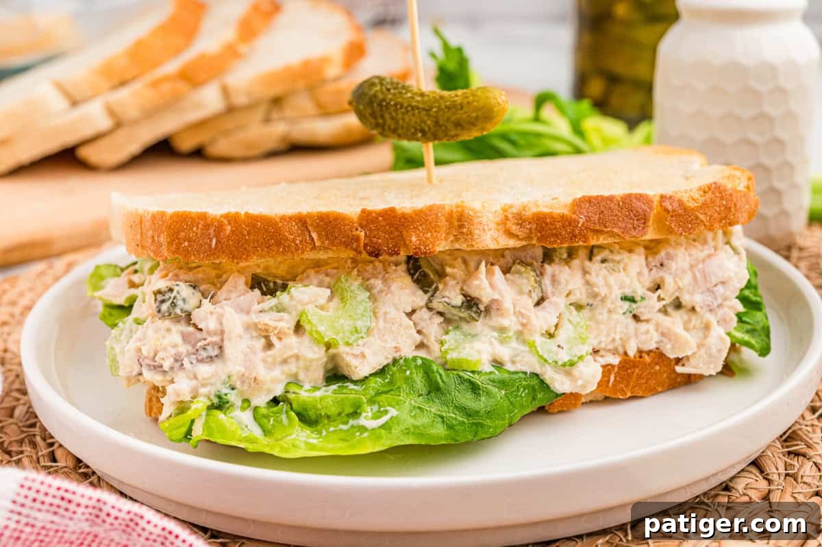 Tuna Salad Recipe for Sandwiches, Wraps, and Lunch 5 A tuna salad sandwich on white bread with lettuce and a baby dill pickle on a pick.