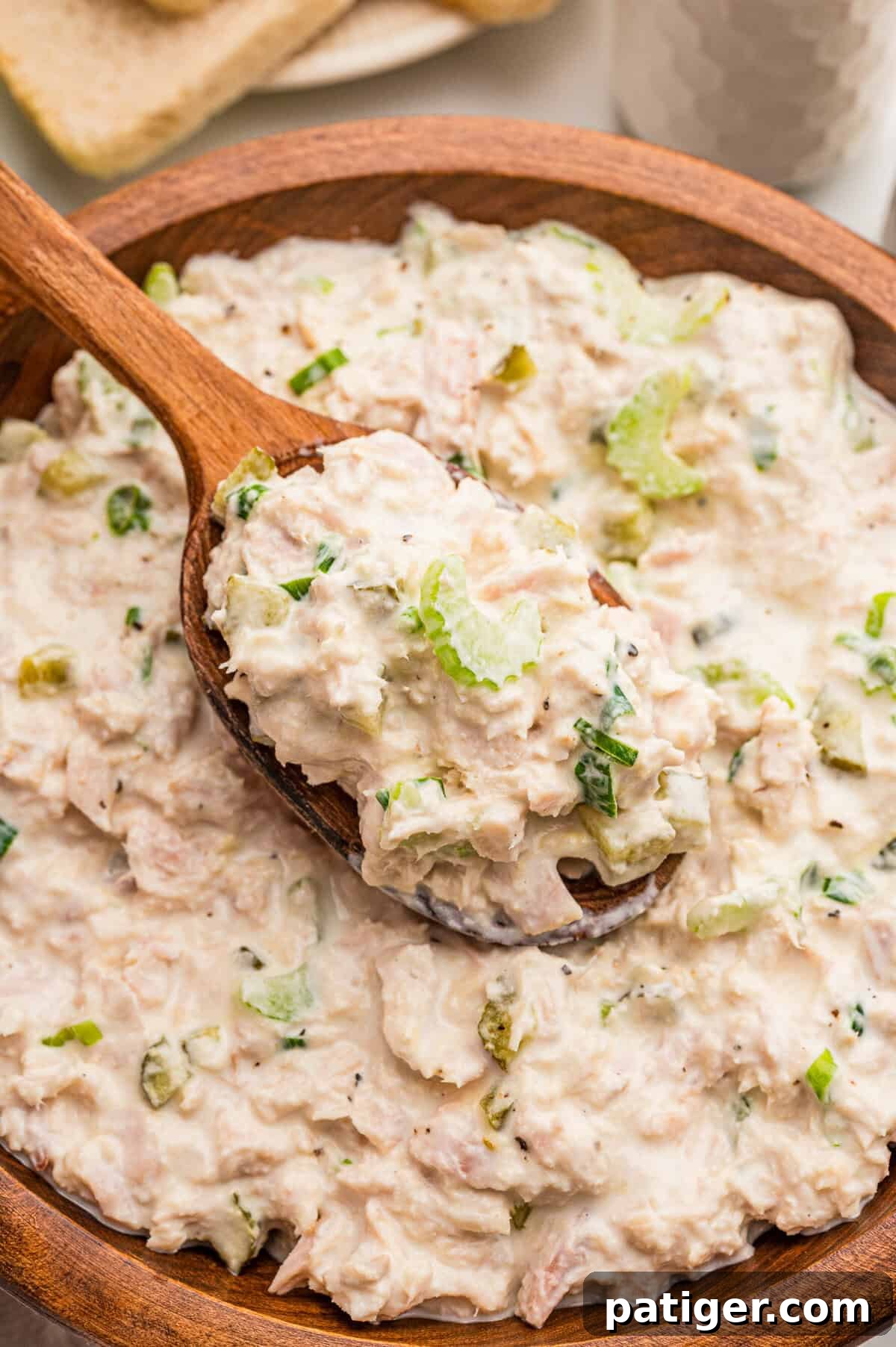 Tuna Salad Recipe for Sandwiches, Wraps, and Lunch 6 A wooden spoon lifting creamy tuna salad from a wooden bowl flecked with celery and pepper.