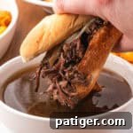 A French Dip Sandwich being dunked into beef au jus.