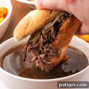 A French Dip Sandwich being dunked into beef au jus.