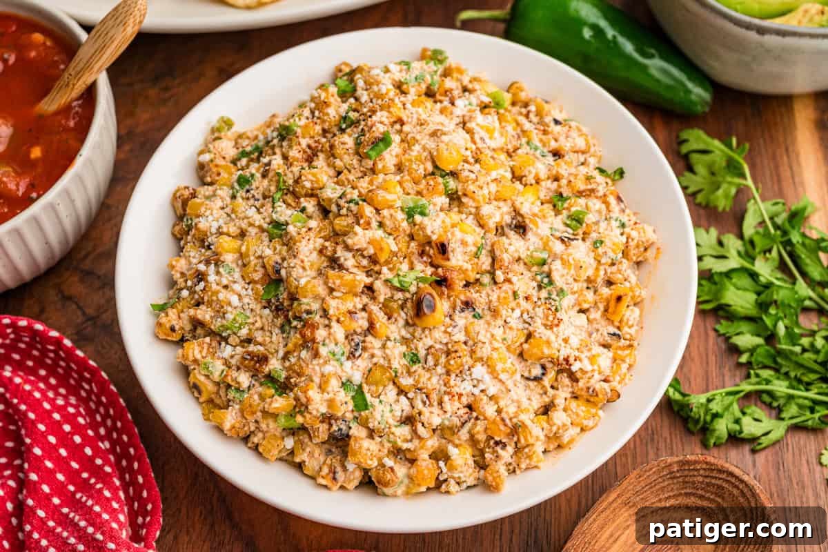 Creamy Mexican Street Corn Dip with Cotija and Lime 2 Mexican street corn dip in a white bowl with charred corn, cotija, and cilantro, tortilla chips and salsa nearby.