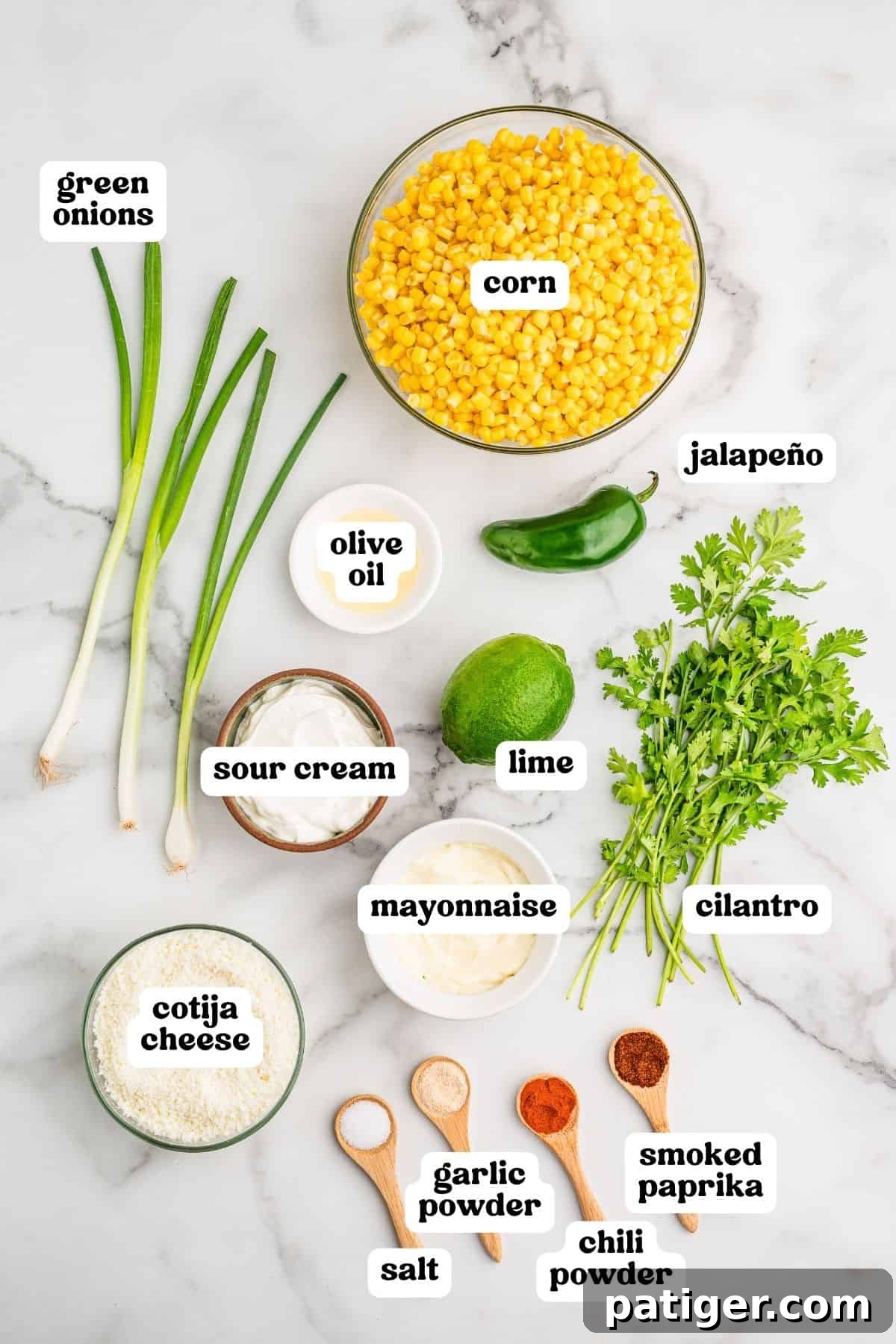 Creamy Mexican Street Corn Dip with Cotija and Lime 3 Labeled ingredients on marble: corn, green onions, jalapeno, olive oil, sour cream, lime, cilantro, mayonnaise, cotija cheese, and spices.
