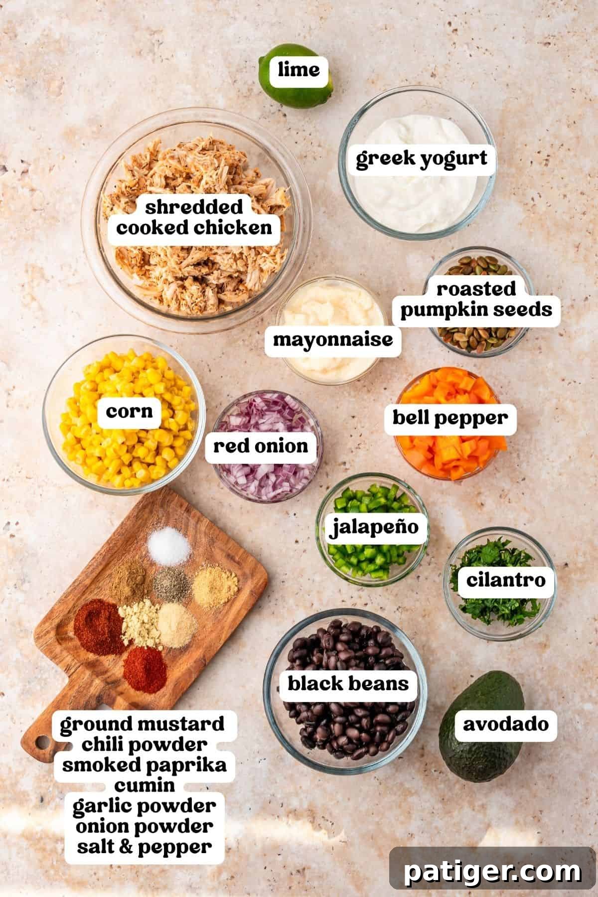 Shredded cooked chicken, Greek yogurt, mayonnaise, corn, black beans, bell pepper, red onion, jalapeno, cilantro, pumpkin seeds, avocado, lime, and spices in bowls.