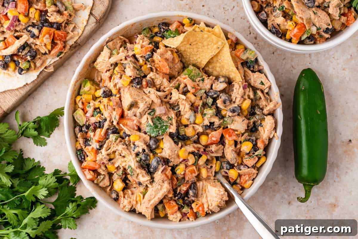 Overhead bowl of chicken salad with corn, black beans, peppers, a tortilla chip, and a fresh jalapeno beside it.