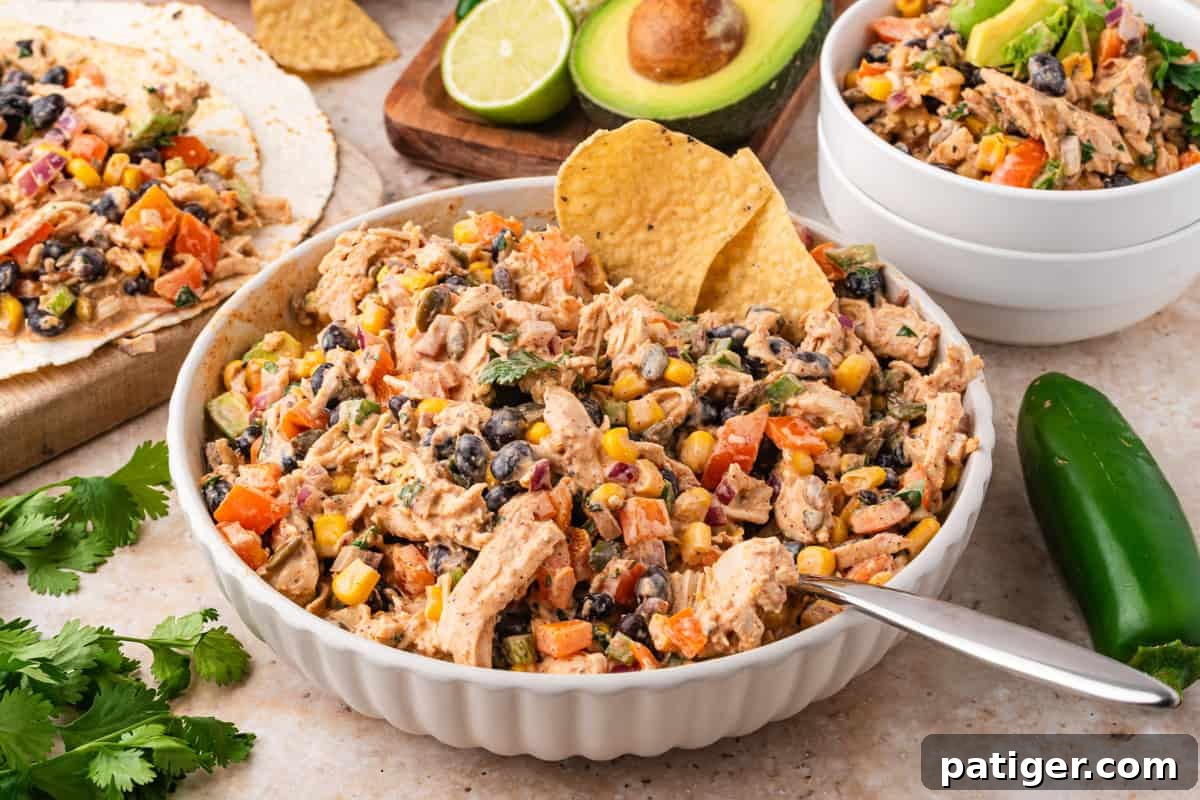 Southwest chicken salad in a white bowl with avocado and lime in the background.