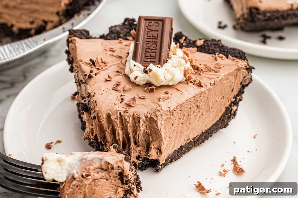 Homemade Hershey's Chocolate Pie Recipe 2 A slice of no bake chocolate pie on a white plate with a forkful on a fork at the edge of the frame.