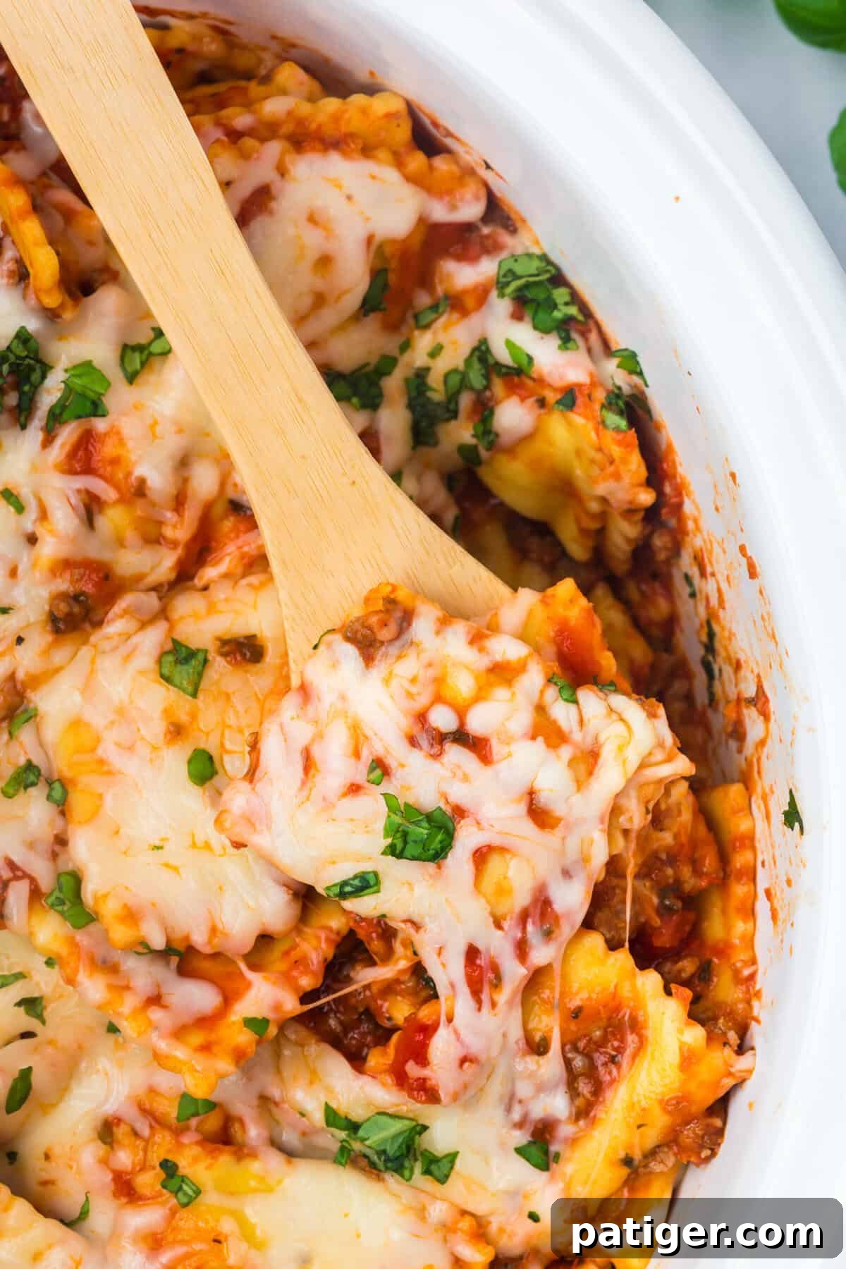 Cheesy crockpot ravioli lasagna topped with basil with a wooden spoon.