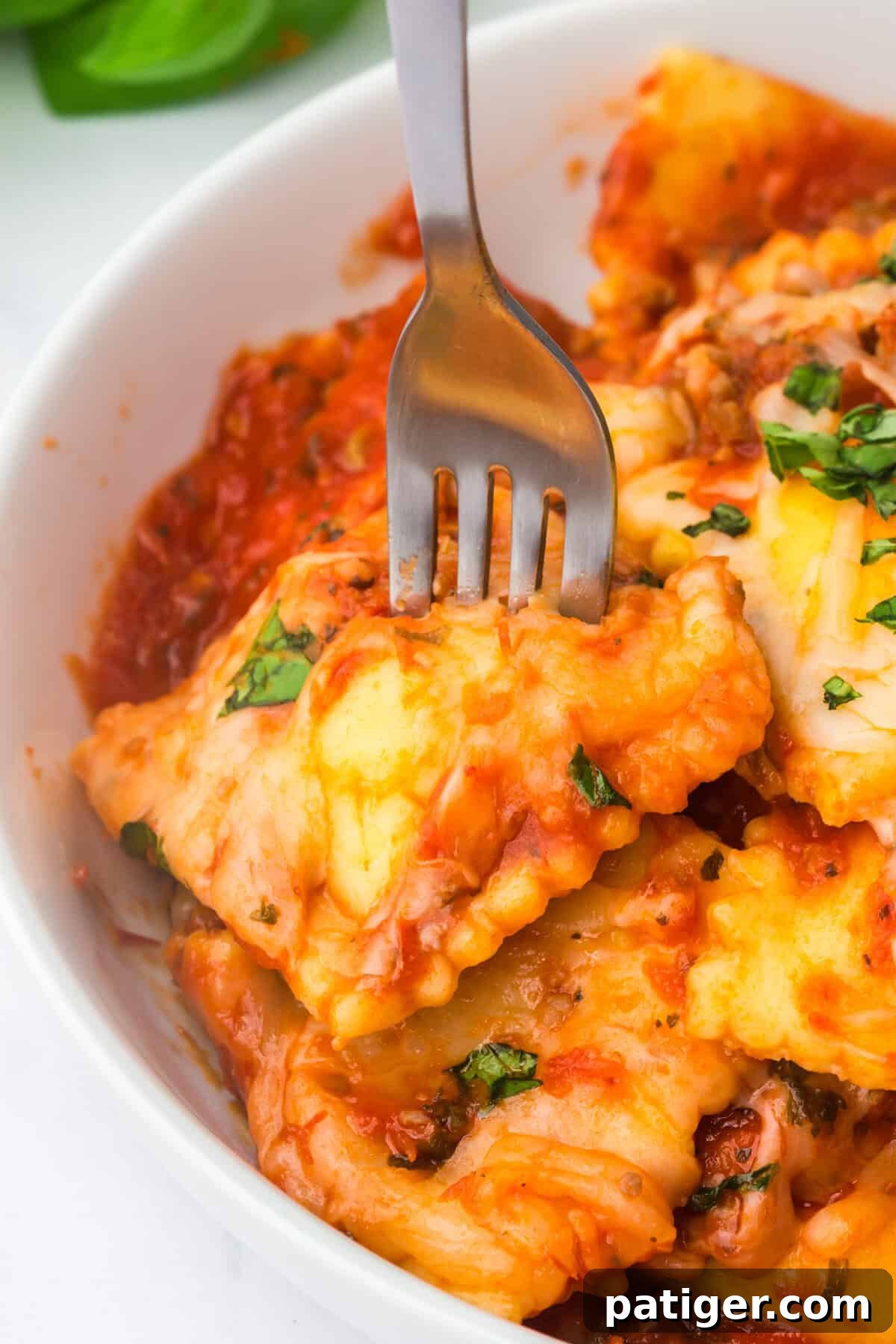 Crockpot ravioli lasagna in a white bowl topped with melted mozzarella and chopped fresh basil.
