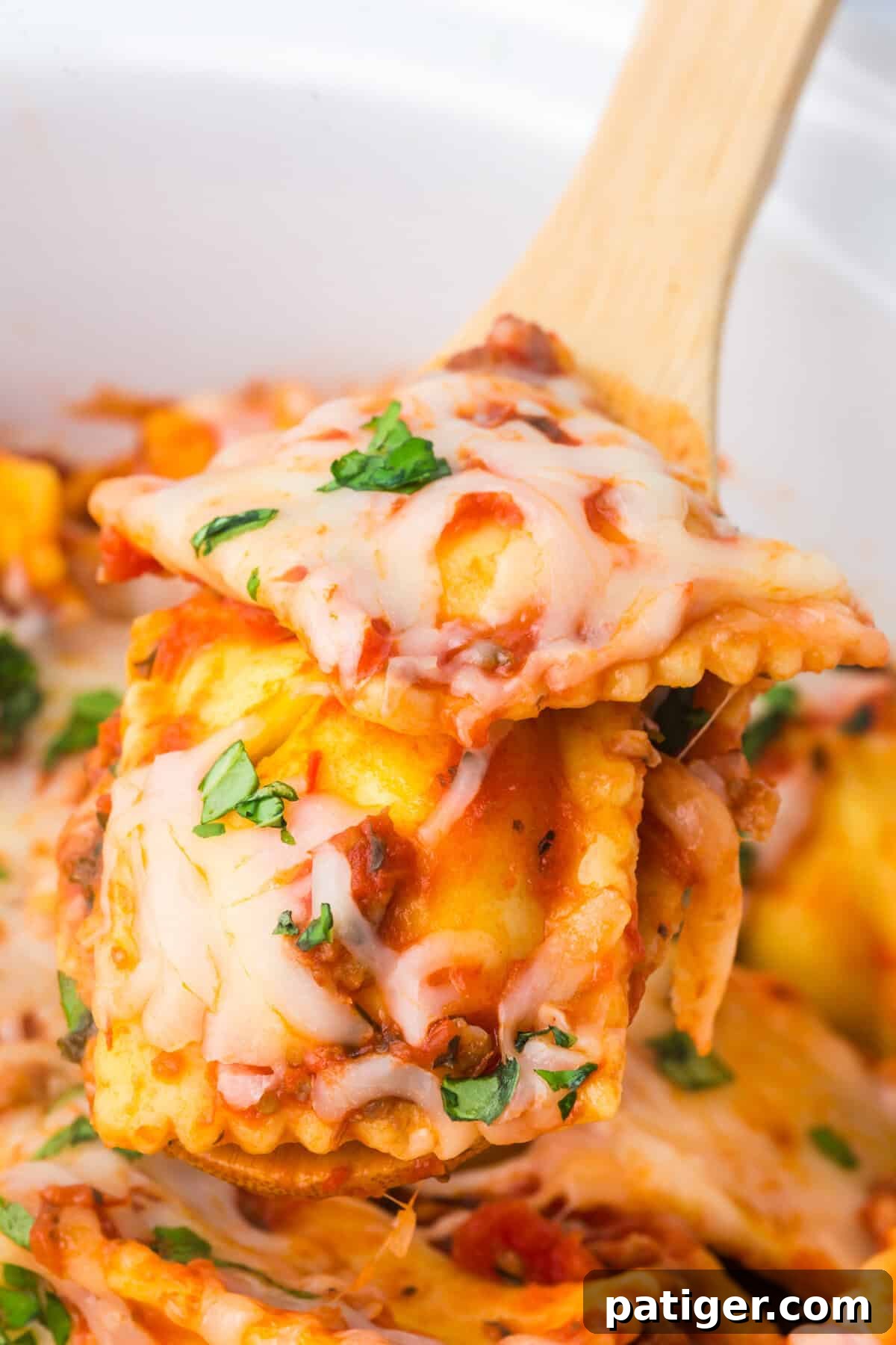 A wooden spoon lifting a cheesy serving of ravioli lasagna from the slow cooker.
