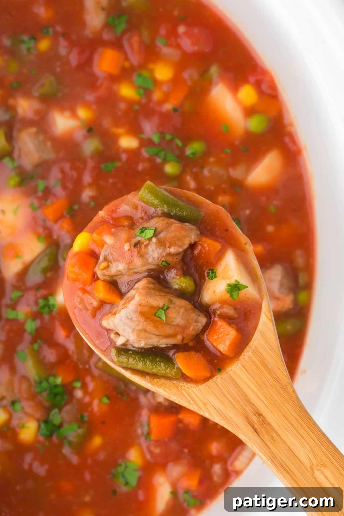 Slow Cooker Vegetable Beef Soup with beef, potatoes, green beans, and carrots being lifted from the crockpot with a wooden spoon. 
