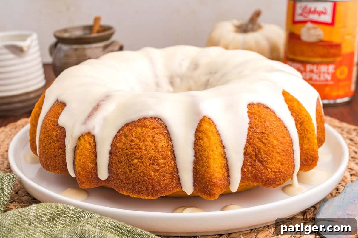 Moist Pumpkin Bundt Cake Made with Cake Mix 12 Whole glazed pumpkin bundt cake on a white plate over a woven mat with a green napkin.