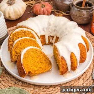 Moist Pumpkin Bundt Cake Made with Cake Mix 13 Glazed pumpkin bundt cake cut into slices on a white plate with small pumpkins and a cinnamon crock behind it.