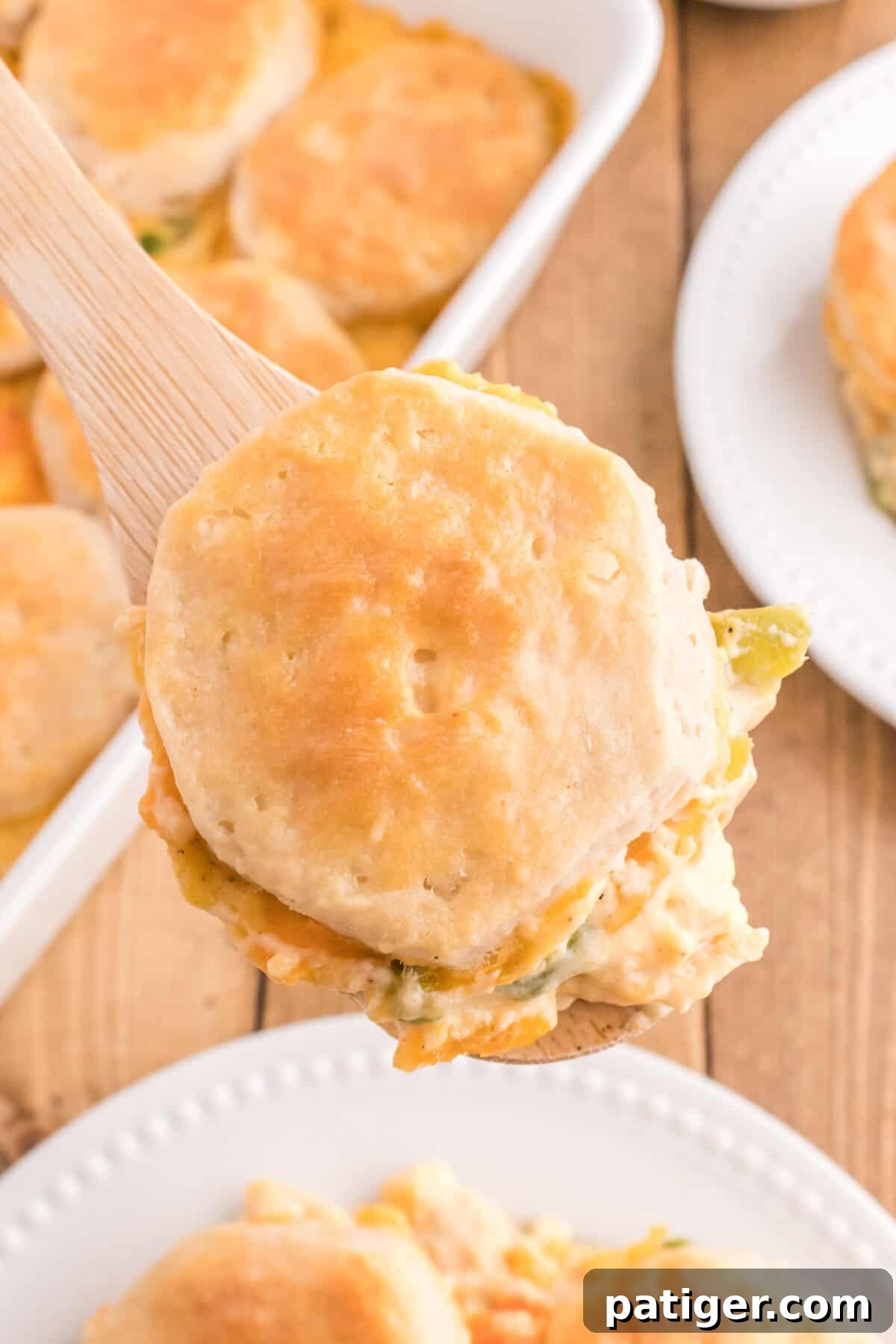One-Pan Chicken Pot Pie Casserole with Biscuits 8 A wooden spoon lifting a biscuit topped portion of creamy chicken and vegetables from the casserole dish.