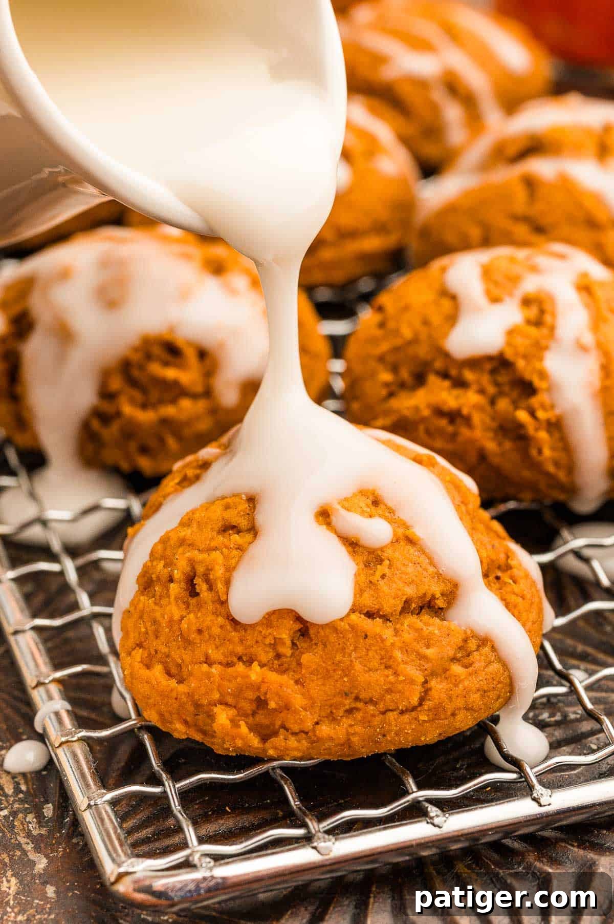 Cake Mix Pumpkin Cookies: Soft Spiced Fall Treats 10 White glaze being poured from a small pitcher over a pumpkin cookie on a wire rack.