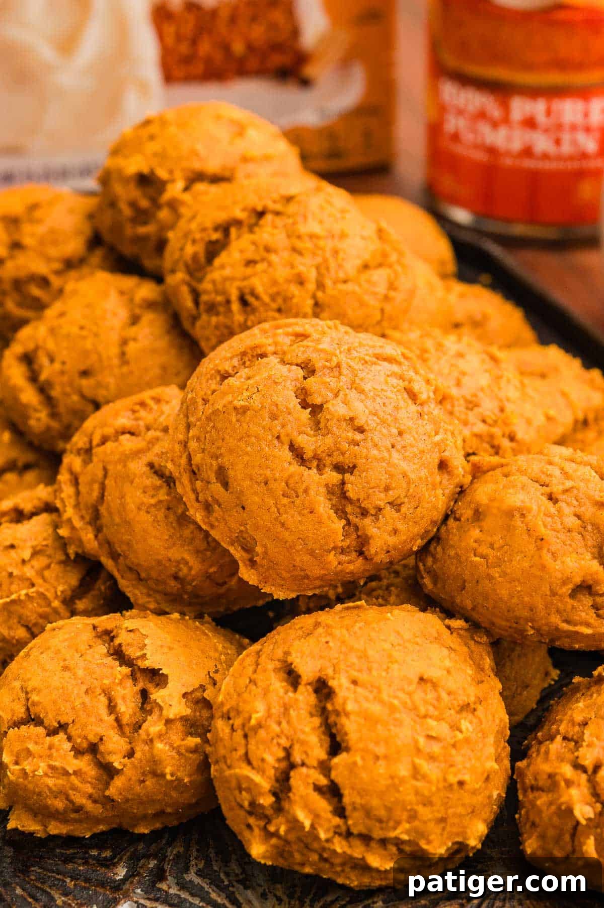 Cake Mix Pumpkin Cookies: Soft Spiced Fall Treats 9 A pile of pumpkin cookies on a dark tray with a spice cake box and pumpkin can behind.