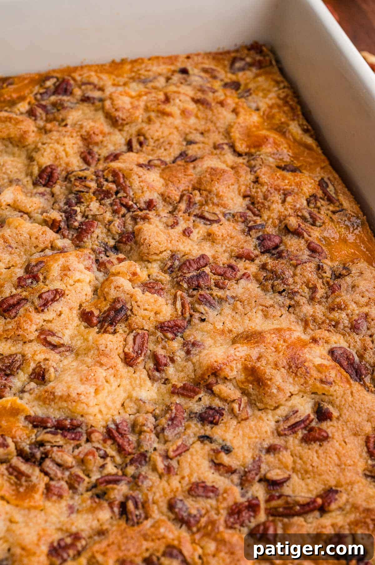Golden baked cake topped with chopped pecans in the corner of a white baking dish.
